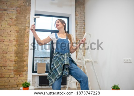 Good mood. Young woman with paint roller in her hand feeling cheerful