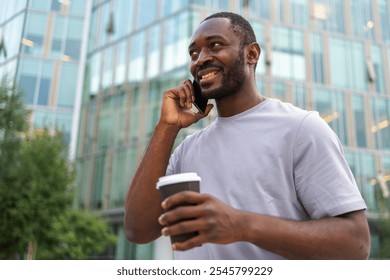 Good morning. African man drinking coffee to go talking on smartphone outdoor. Man with cell phone paper cup walking on street. Man making answering call by cellphone having conversation by mobile - Powered by Shutterstock