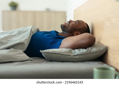 Good Morning. Cheerful Black Guy Lying In Cozy Bed Holding Hands Behind Head Smiling Looking At Ceiling Resting And Relaxing In Modern Bedroom At Home. Healthy Sleeping Routine Concept