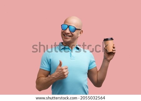 Good morning. Cheerful smiling bald unshaven homosexual man enjoys his hot coffee, shows thumb up, holds take-away cup, gay friendly, wears blue shirt and sunglasses, stands on pink background Stock photo © 
