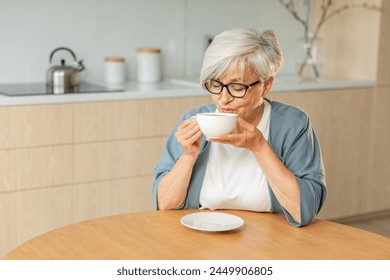 Good morning. Comfort relaxed senior old elderly woman grandmother drinking hot beverage tea coffee in kitchen at home. Mature woman resting enjoy calm morning at modern home alone. Pension concept - Powered by Shutterstock