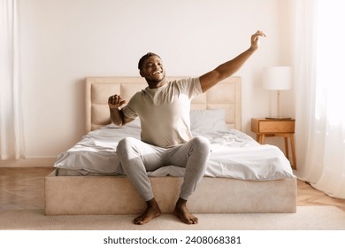 Good Morning. Happy Black Man Waking Up And Stretching Arms With Toothy Smile, Relaxed After Great Rest, Sitting In Bed In Modern Bedroom Interior. Start Of New Day, Rest And Wellness Concept - Powered by Shutterstock