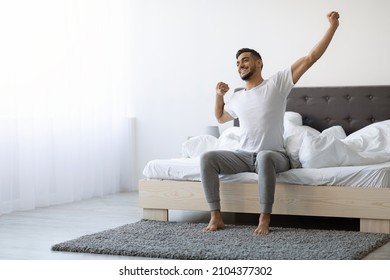 Good Morning. Happy Millennial Arab Guy Sitting On Bed And Stretching After Good Sleep, Handsome Smiling Young Middle Eastern Man Relaxing In Cozy Bedroom, Enjoying Home Comfort, Copy Space