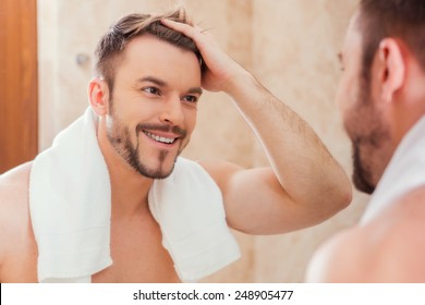 Good Morning To Me. Handsome Young Man Touching His Hair With Hand And Smiling While Standing In Front Of The Mirror