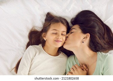 Good Morning, My Sweet Little Angel. Mother Wakes Up Her Daughter And Kisses Her On The Cheek. Happy Family Cuddling On A Soft White Pillow In A Cosy, Warm Bed, High Angle Shot. Love And Care Concept