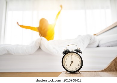 Good Morning New Day. Alarm Clock Wake Up And Woman Sitting Body Stretch On Bed Beside Window In Bedroom