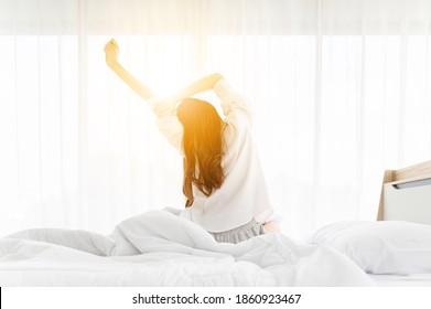 Good Morning New Day. Asian Woman Wake Up And Sitting Body Stretch On Bed Beside Window In Bedroom