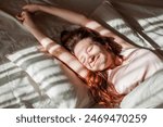 Good morning, new day, weekend, holiday. Happy Young Woman sets on Bed, teen Girl Stretching arms after sleep and enjoying morning in cozy comfort bedroom interior