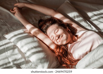 Good morning, new day, weekend, holiday. Happy Young Woman sets on Bed, teen Girl Stretching arms after sleep and enjoying morning in cozy comfort bedroom interior