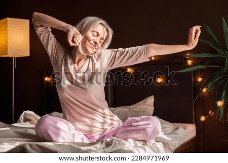 Good morning, new day, weekend, holiday. Happy middle aged woman sits on bed, lady stretching arms after sleep and enjoying morning in cozy comfort bedroom interior, free space 商業照片 © 