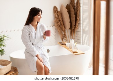 Good Morning. Relaxed Brunette Woman Drinking Coffee Holding Cup Sitting On Bathtub Wearing White Bathrobe In Luxury Bathroom Indoor. Pampering And Beauty Rituals Concept - Powered by Shutterstock