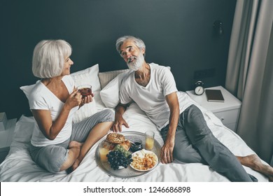 Good morning! Senior family couple enjoying breakfast in bed. - Powered by Shutterstock