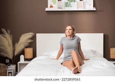 Good morning time cheerful blond girl after sleep laying on bed leaning on hands smiling looking at winndow preparing for good light hard day.