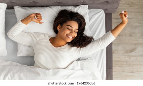 Good Morning. Top Above View Of Satisfied Young African American Woman Stretching After Wakeup, Feeling Good, Charming Black Lady Sleeping And Lying On The White Bedsheets At Home, Relaxing In Bedroom