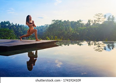 Good morning with yoga meditating on sunrise background. Active woman in bikini practicing at villa poolside to keep fit and health. Woman fitness training, sport activity on summer family holiday. - Powered by Shutterstock