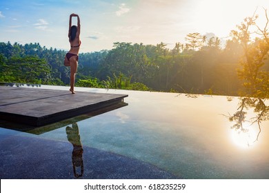 Good morning with yoga meditating on sunrise background. Active woman in bikini practicing on villa poolside to keep fit and health. Woman fitness training, sport activity on summer family holiday. - Powered by Shutterstock