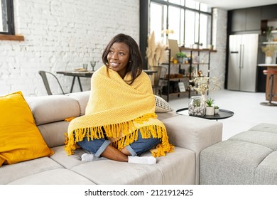 Good morning. Young multiracial teenage girl covered in a cozy yellow soft blanket staying at home at the warm sofa, looking in the window, feeling happy and blessed