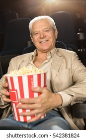 Good Movie Gives Him Smiles. Cheerful Senior Man Smiling Joyfully Holding His Popcorn While Relaxing At The Movie Theatre Entertainment Hobby Leisure Happiness People Concept