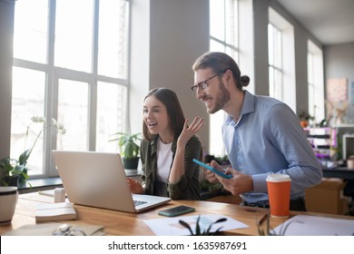 Good news. Enthusiastic young man with a tablet in his hands and a girl with long hair, standing at a table in front of a laptop and looking admiringly at the screen, in excellent mood. - Shutterstock ID 1635987691