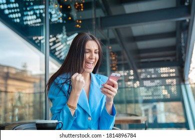 Good news. Excited happy Indian girl celebrating online win, holding phone, looking at camera sitting at home balcony, overjoyed successful lucky young woman rejoicing victory, triumph, laughing