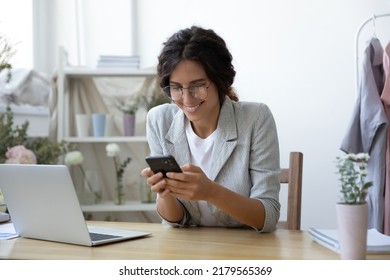 Good News. Excited Young Female Self Employed Clothing Designer Sitting At Work Desk Focused On Mobile Phone Screen. Woman Flower Arranger Reading Email With Profitable Offer From Potential Customer