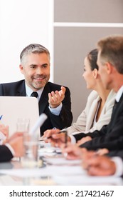 Good News For Our Company! Business People In Formalwear Discussing Something While Sitting Together At The Table