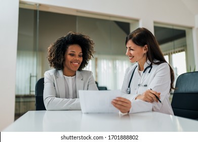 Good news! Smiling female patient and doctor looking at paper document.