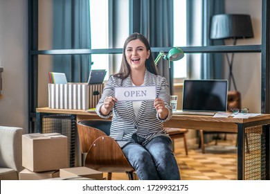 Good news. Young woman in a striped jacket sitting on the chair and looking joyful - Shutterstock ID 1729932175