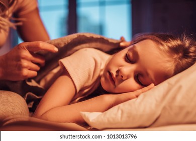 Good night, princess! Attractive young woman with little cute girl are spending time together at home. Mom is putting daughter to bed. Happy family concept. Mother's day. - Powered by Shutterstock