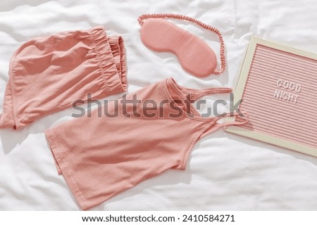 Good night wishes concept, Pink woman pajamas, sleep eye mask on white bed sheet. Felt board with text Good night. Aesthetic lifestyle flat lay photo, comfort and stylish pajama wear or clothes
