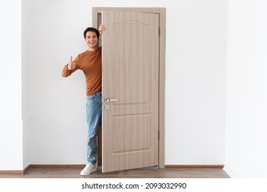 Good Offer. Portrait of cheerful young guy standing in doorway of his apartment, smiling millennial male homeowner holding ajar door looking out, greeting visitor, showing thumbs up like sign gesture - Powered by Shutterstock