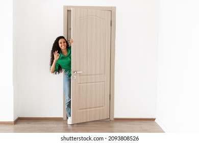 Good Offer. Portrait of cheerful young lady standing in doorway of her apartment, smiling millennial female homeowner holding ajar door looking out, greeting visitor, showing okay cool sign gesture - Powered by Shutterstock