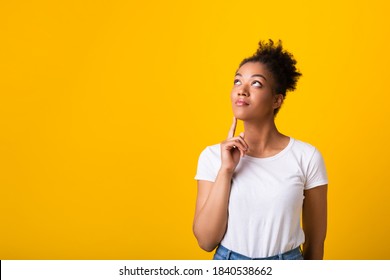 Good Offer. Portrait Of Dreamy African American Lady Looking Up At Copy Space, Touching Her Chin With Finger, Isolated Over Yellow Studio Background. Pensive Black Woman Thinking And Making Decision