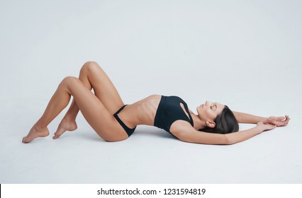 Good Posture. Photo Of A Young Girl In Black Underwear Laying Down On The White Surface.