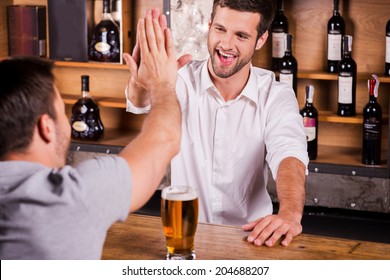 It Is Good To See You Again! Rear View Of Male Customer Talking To Bartender While Sitting At The Bar Counter 