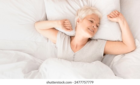 Good sleep. Pleased senior woman stretching in bed, awakening morning moment, top view, panorama with empty space - Powered by Shutterstock