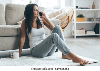 Good Talk With Boyfriend. Attractive Young Woman Talking On Mobile Phone And Smiling While Sitting On The Carpet At Home 