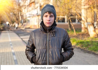A good teenager resting in the city at sunset. Beginning in winter, he is dressed in a winter hat and a jacket - Shutterstock ID 775534504