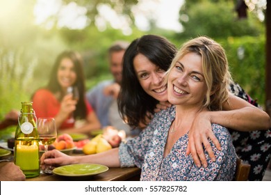 Good Time For A Group Of Friends Sharing A Meal On A Terrace In Summer, Focus On Two Beautiful Women Looking At Camera. Shot With Flare