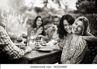 Good Time For A Group Of Friends Sharing A Meal On A Terrace In Summer, Focus On Two Beautiful Women Looking At Camera. Black And White