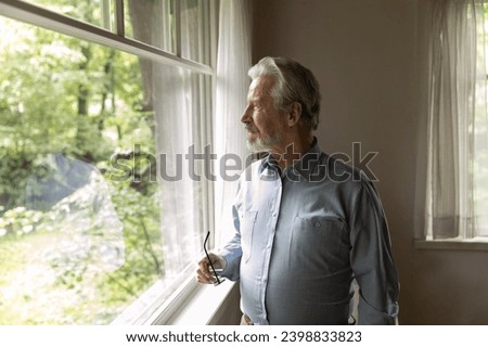 Good vision on retirement. Hoary elderly male take glasses off look away get used to sharp eyesight after laser surgery. Pensive older man stand at home by window admire sunny day outside. Copy space