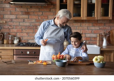 Good work my boy. Smiling older grandpa praise preteen grandson assisting him at kitchen cutting fresh salad of vegetable ingredients. Skilled tween kid in apron help granddad in cooking dietary food - Powered by Shutterstock