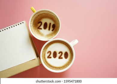 Goodbye 2019 Hello 2020 Holidays Food Art Theme Coffee Cup With Number 2020 On Frothy Surface, Another One With 2019 At The Bottom Of Cup Over Pink Background With Blank Calendar. (space For Text)