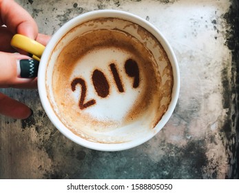 Goodbye 2019 Theme Coffee Cup With Coffee Stain And Number 2019 At The Bottom Of Cup On Grey Cement Background With Blurred Female Fingers. New Year New You, Holidays Food Art Concept. (top View)