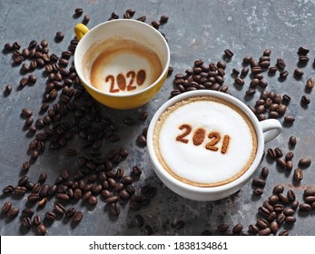 Goodbye 2020, Hello 2021 Holidays Food Art Theme Coffee Cups With Number 2021 And 2020 On Frothy Surface Flat Lay On Grey Cement Background With Coffee Beans. Holidays Food Art For Happy New Year.