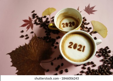 Goodbye 2020, Hello 2021 Holidays Food Art Theme Coffee Cups With Number 2021 And 2020 On Frothy Surface Flat Lay On Pink Background With Coffee Beans, Dried Yellow Ginkgo Biloba Leaf, Red Maple Leaf.