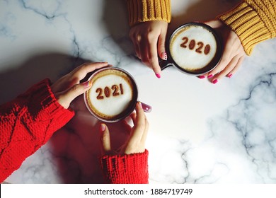 Goodbye 2020, Hello 2021 Theme Coffee Cup With Number 2021 On Frothy Surface In Female Hands Holding And Another One With Number 2020 On Frothy Surface Over Marble Table Background. Holidays Food Art.