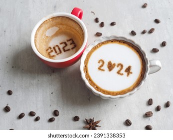 Goodbye 2023 Hello 2024 holidays food art theme coffee cup with number 2024 on frothy surface, another one with 2023 at the bottom over rustic grey cement background with coffee beans and star anise.