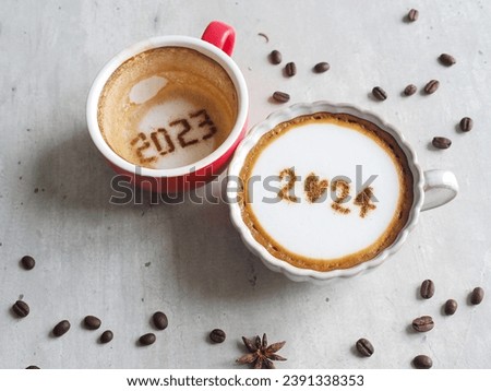 Goodbye 2023 Hello 2024 holidays food art theme coffee cup with number 2024 on frothy surface, another one with 2023 at the bottom over rustic grey cement background with coffee beans and star anise.