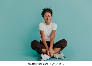 Good-humoured african american girl sitting with crossed legs. Front view of wonderful black female model posing on turquoise background. - Powered by Shutterstock